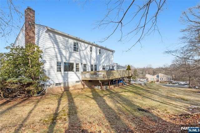 back of house with a chimney, a deck, and a lawn