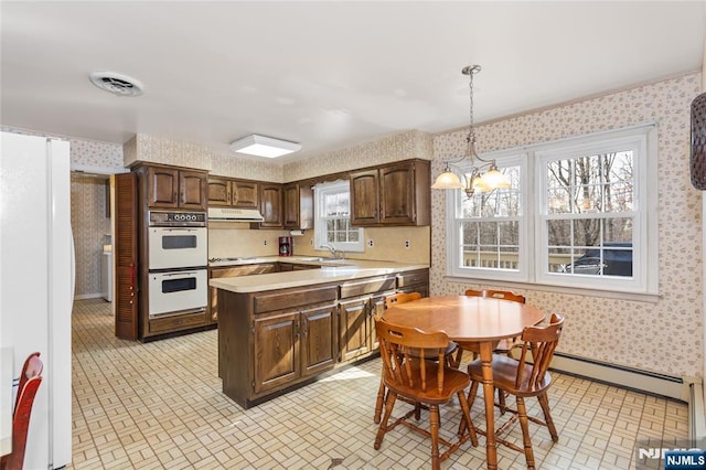 kitchen featuring pendant lighting, light countertops, white appliances, under cabinet range hood, and wallpapered walls