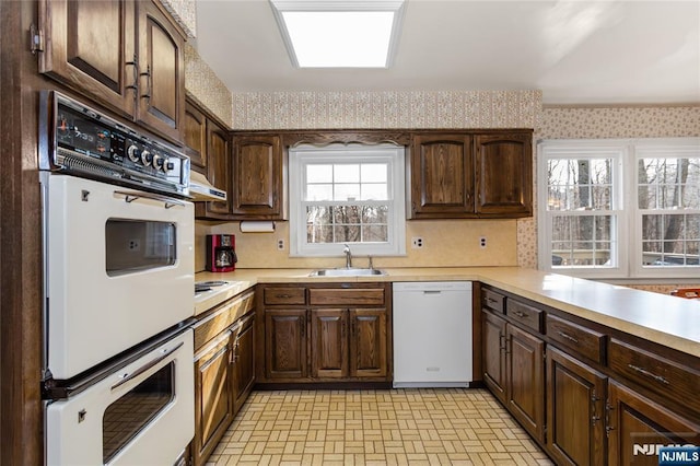 kitchen featuring white appliances, wallpapered walls, a sink, light countertops, and brick patterned floor