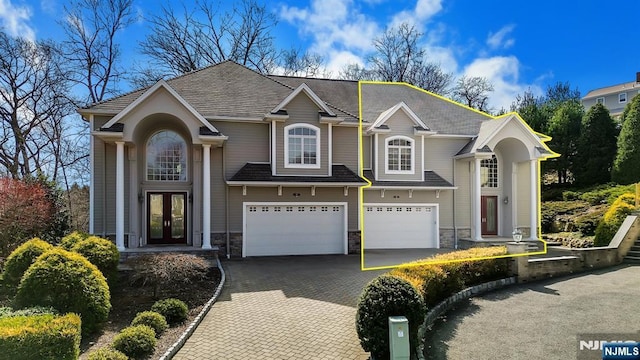 traditional home with french doors, stone siding, a garage, and decorative driveway