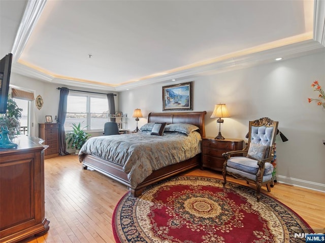 bedroom featuring ornamental molding, light wood finished floors, a raised ceiling, and baseboards