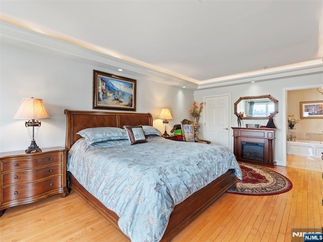 bedroom featuring ensuite bath, a glass covered fireplace, and light wood-style floors