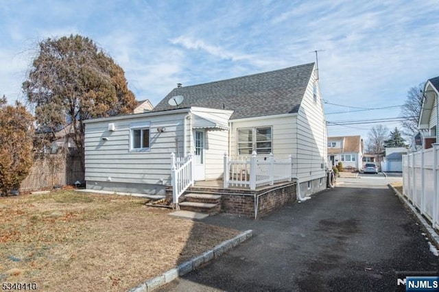 bungalow-style home with driveway, fence, a front lawn, and roof with shingles