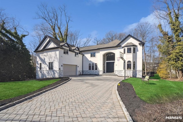 french country style house with decorative driveway, stucco siding, a front yard, a garage, and stone siding