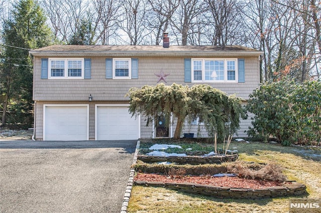 view of front facade featuring driveway, a chimney, and an attached garage