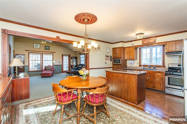 kitchen with brown cabinets, appliances with stainless steel finishes, open floor plan, a kitchen island, and under cabinet range hood