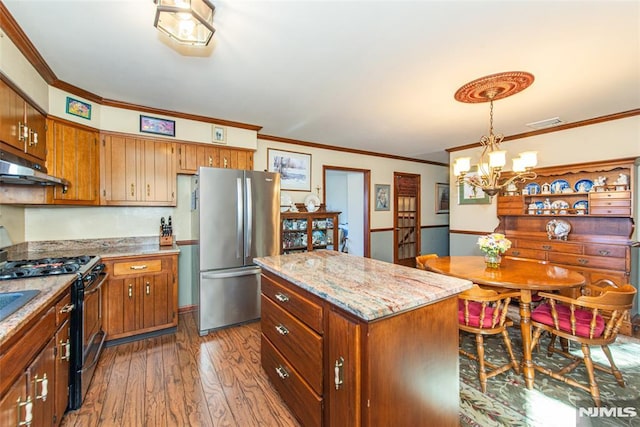 kitchen featuring black range with gas cooktop, brown cabinetry, dark wood finished floors, freestanding refrigerator, and under cabinet range hood