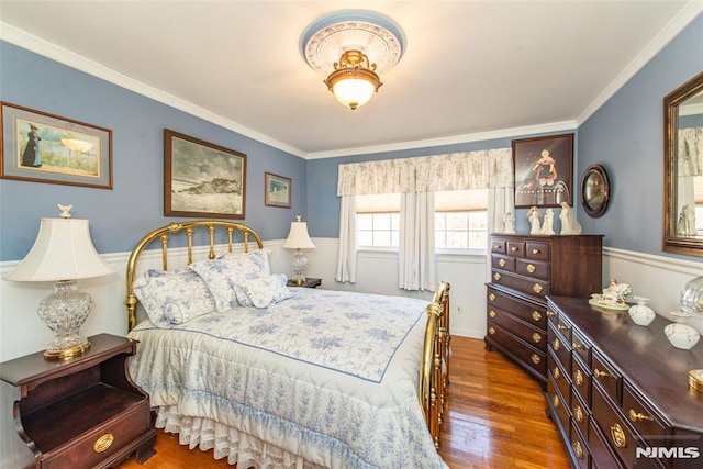 bedroom featuring a wainscoted wall, ornamental molding, and wood finished floors