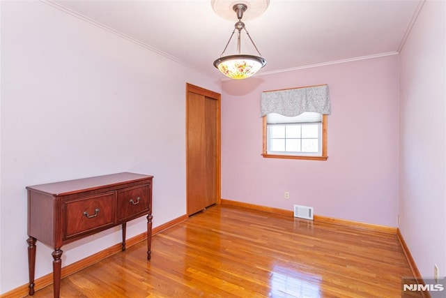 empty room with baseboards, light wood finished floors, visible vents, and crown molding