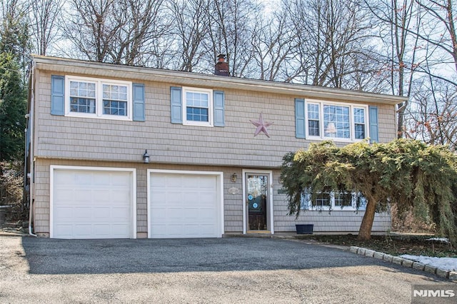 view of front of house featuring driveway, an attached garage, and a chimney