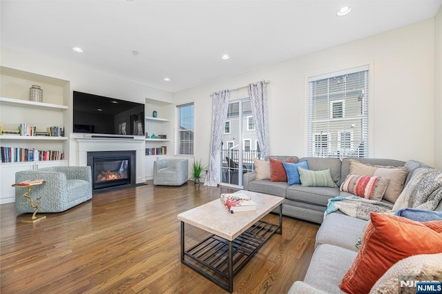 living room featuring a glass covered fireplace, built in shelves, wood finished floors, and recessed lighting