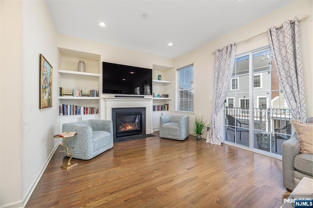 sitting room featuring baseboards, built in features, a fireplace with flush hearth, recessed lighting, and wood finished floors