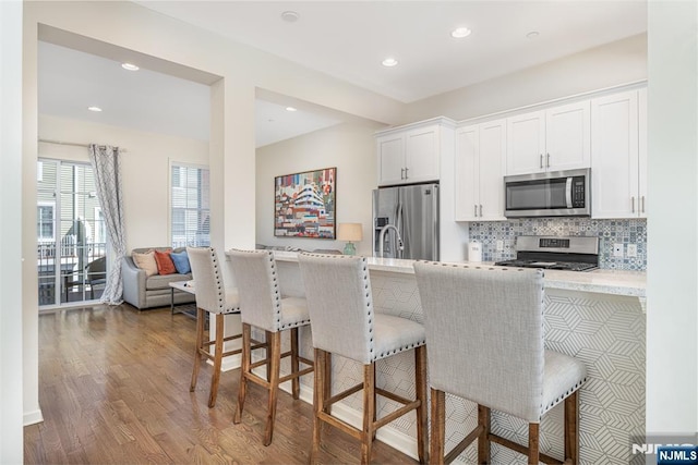 kitchen with backsplash, a breakfast bar area, appliances with stainless steel finishes, wood finished floors, and white cabinetry