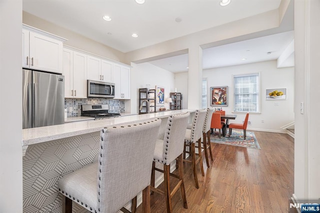 kitchen featuring light stone counters, wood finished floors, stainless steel appliances, white cabinetry, and backsplash