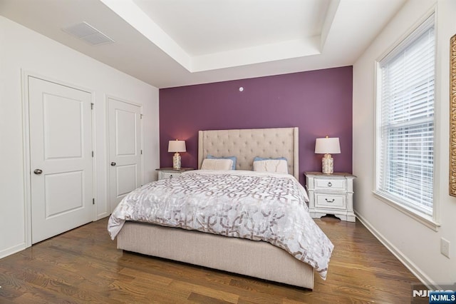 bedroom with a tray ceiling, wood finished floors, visible vents, and baseboards