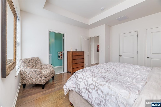 bedroom with visible vents, ensuite bath, wood finished floors, baseboards, and a raised ceiling