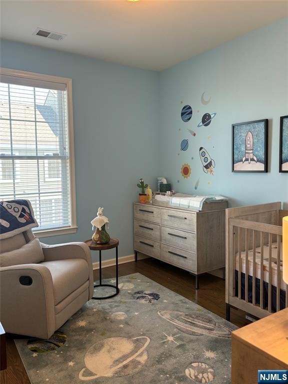 bedroom with dark wood finished floors, a crib, baseboards, and visible vents