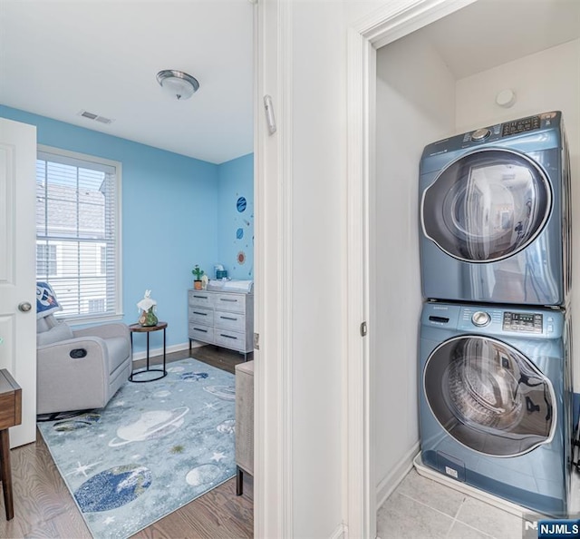 laundry room with visible vents, stacked washer and clothes dryer, wood finished floors, baseboards, and laundry area