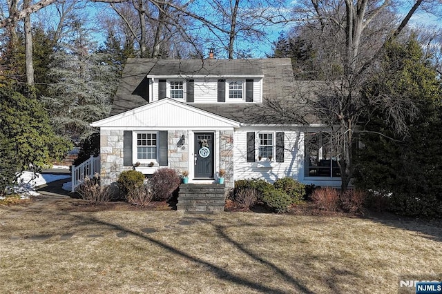 view of front of home featuring a front yard, stone siding, and roof with shingles