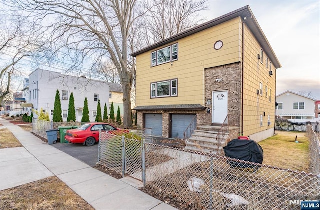 view of front of property featuring a garage, driveway, brick siding, and a fenced front yard