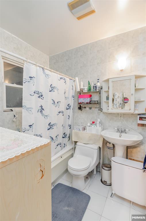 full bath featuring shower / bath combo, visible vents, toilet, tile patterned flooring, and tile walls