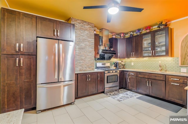 kitchen with decorative backsplash, wall chimney exhaust hood, glass insert cabinets, appliances with stainless steel finishes, and a sink