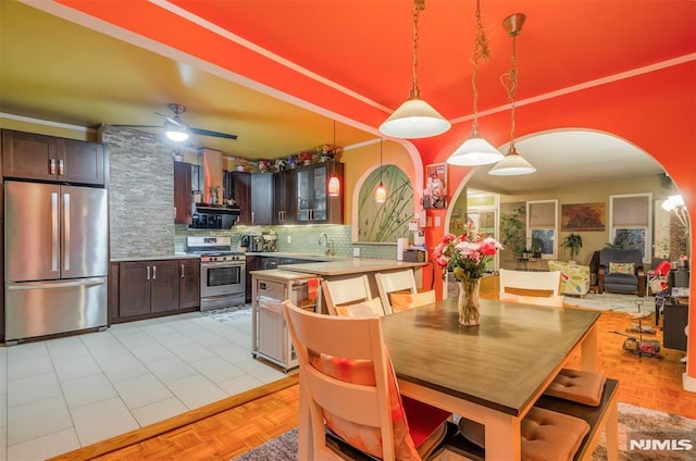 kitchen featuring arched walkways, backsplash, stainless steel appliances, dark brown cabinets, and a sink