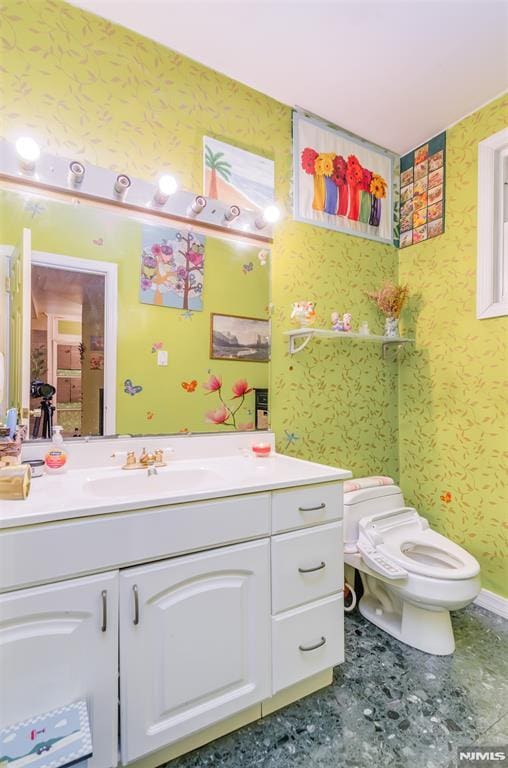 bathroom featuring baseboards, vanity, toilet, and wallpapered walls