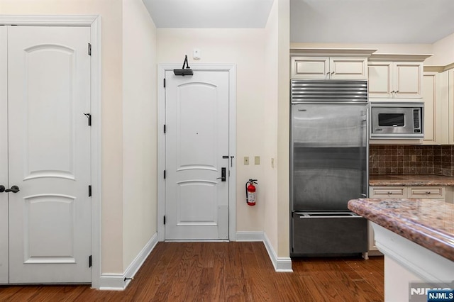 kitchen featuring built in appliances, cream cabinetry, dark wood-style flooring, and decorative backsplash