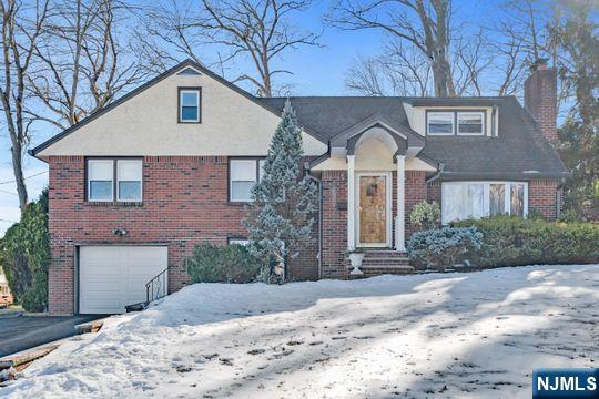 view of front of home with a garage, brick siding, driveway, and a chimney