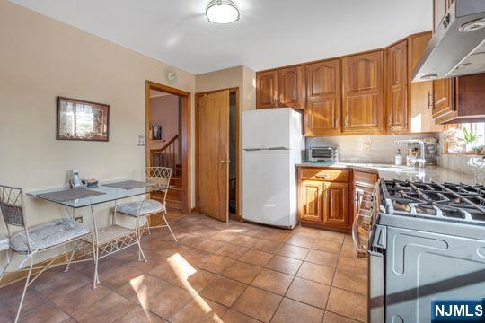 kitchen with under cabinet range hood, light countertops, freestanding refrigerator, brown cabinets, and stainless steel gas stove