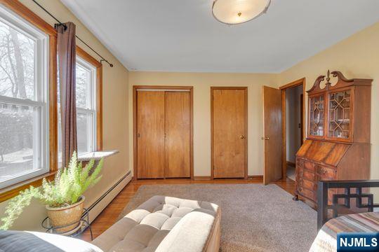 bedroom with light wood-style floors, baseboard heating, and multiple closets