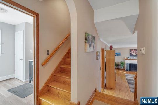 staircase featuring baseboards, a fireplace, arched walkways, and wood finished floors