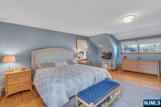 bedroom with a baseboard radiator, vaulted ceiling, and wood finished floors