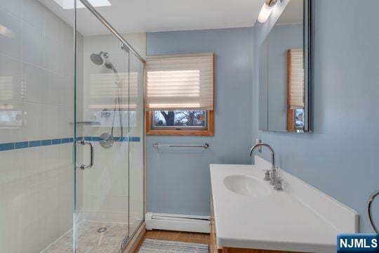 full bath with a stall shower, a baseboard radiator, a skylight, and vanity