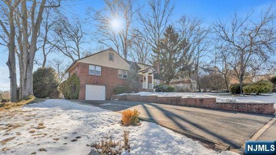 view of snow covered exterior with aphalt driveway, a chimney, and a garage