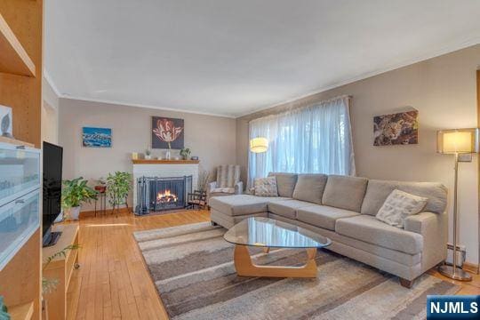 living room with a warm lit fireplace, wood-type flooring, and ornamental molding