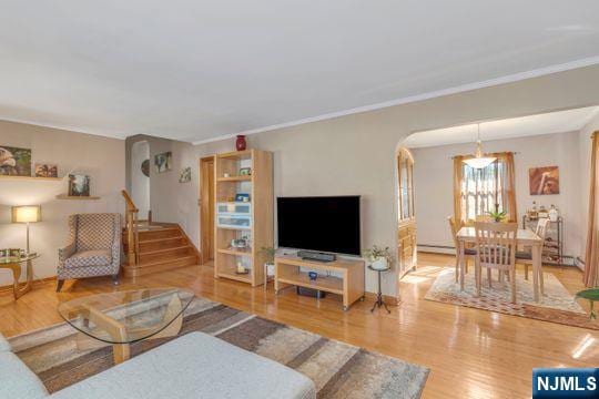 living area with stairs, arched walkways, wood finished floors, and ornamental molding