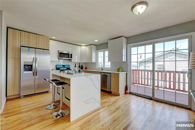 kitchen featuring modern cabinets, appliances with stainless steel finishes, a center island, light wood-style floors, and a sink