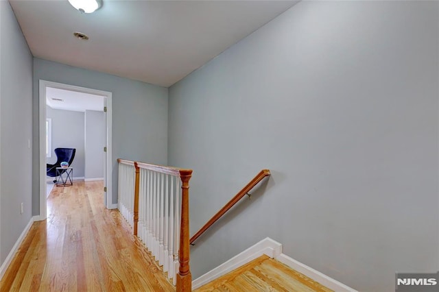 hallway with light wood finished floors, baseboards, and an upstairs landing