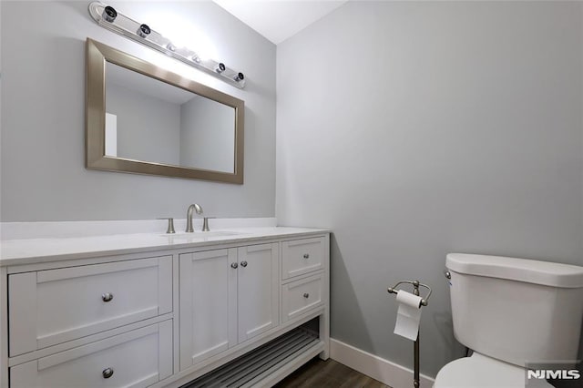 bathroom featuring toilet, baseboards, wood finished floors, and vanity