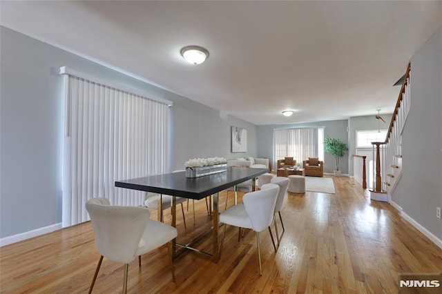 dining room featuring light wood-type flooring, stairway, and baseboards