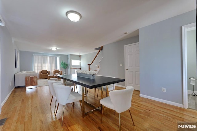 dining area featuring visible vents, baseboards, stairway, and light wood finished floors