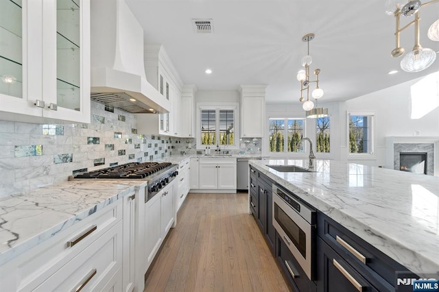 kitchen with stainless steel appliances, custom range hood, visible vents, white cabinetry, and a sink