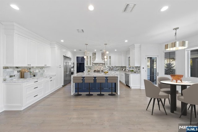 kitchen featuring visible vents, appliances with stainless steel finishes, white cabinets, premium range hood, and a kitchen bar