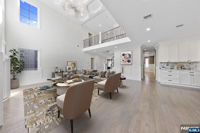 living room featuring light wood-style flooring, visible vents, a decorative wall, and wainscoting