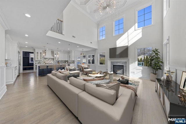 living room featuring a notable chandelier, a decorative wall, a high end fireplace, light wood finished floors, and crown molding