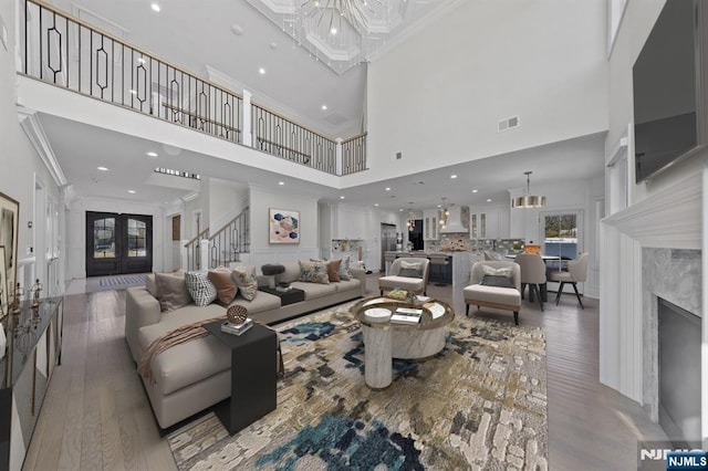 living area with a notable chandelier, wood finished floors, ornamental molding, french doors, and stairway