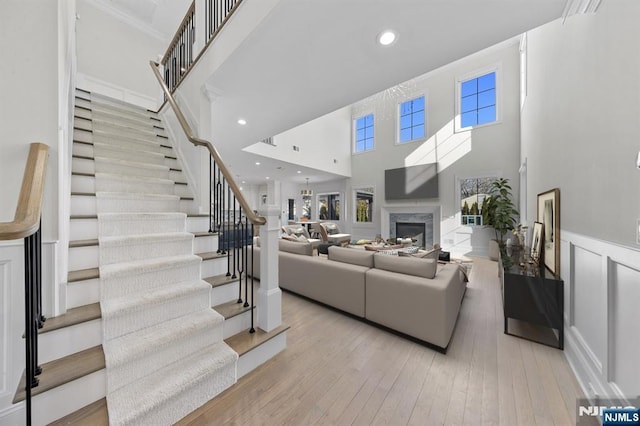 living room featuring light wood finished floors, wainscoting, stairway, a high ceiling, and a fireplace