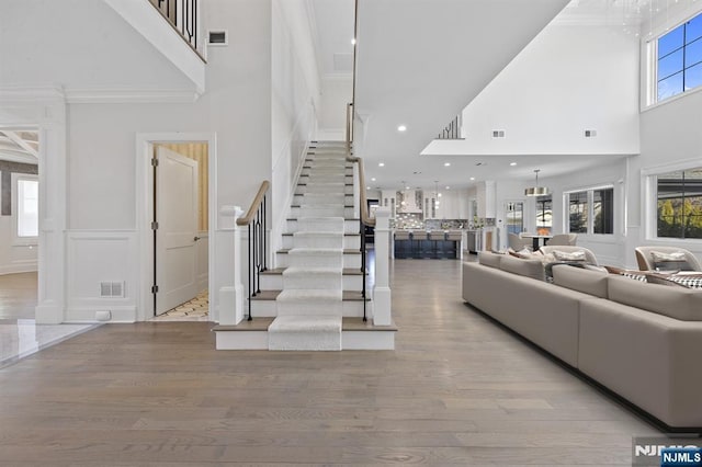 living room featuring a decorative wall, a wainscoted wall, wood finished floors, visible vents, and stairs